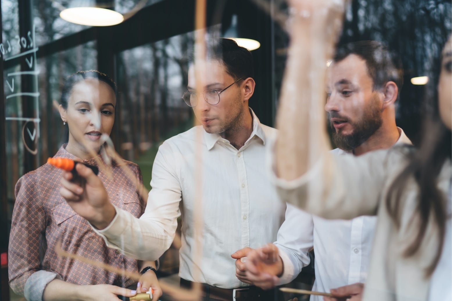 Three colleagues collaborating at a glass board, with one person writing notes using an orange marker.
