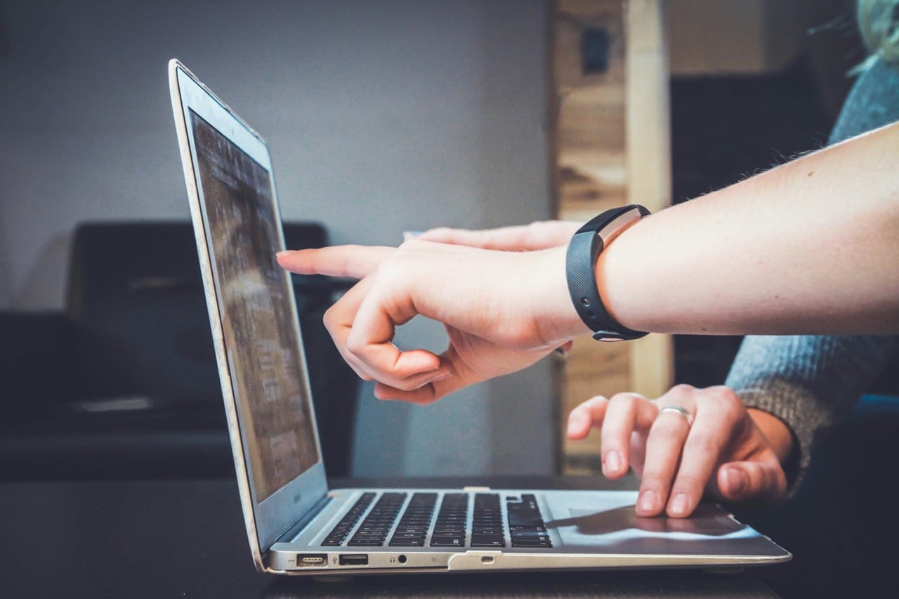 Person wearing fitness tracker pointing at laptop screen while another hand rests on the touchpad.