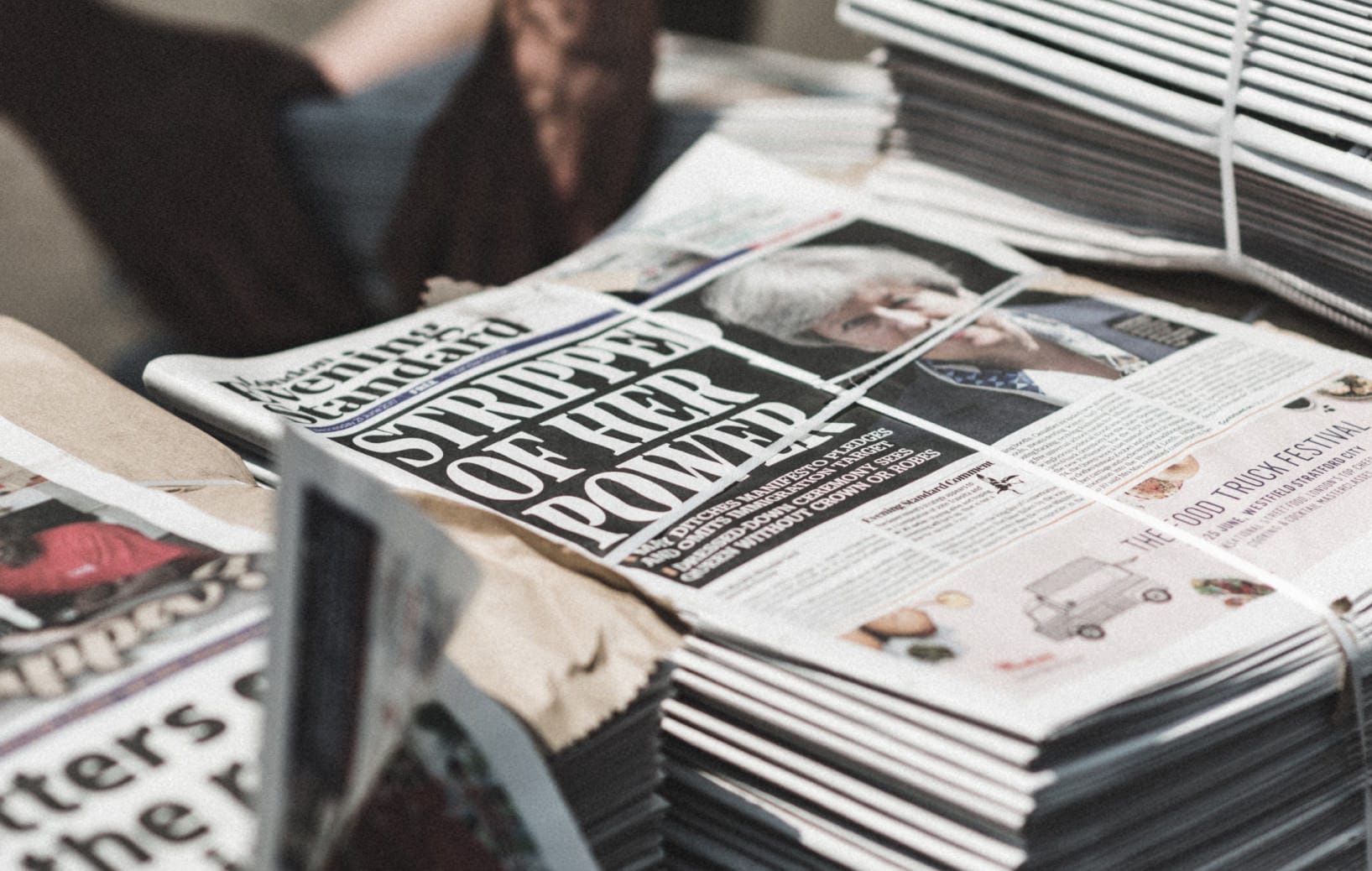 Stack of Evening Standard newspapers with headline "STRIP OF HER POWER" visible on the front page.
