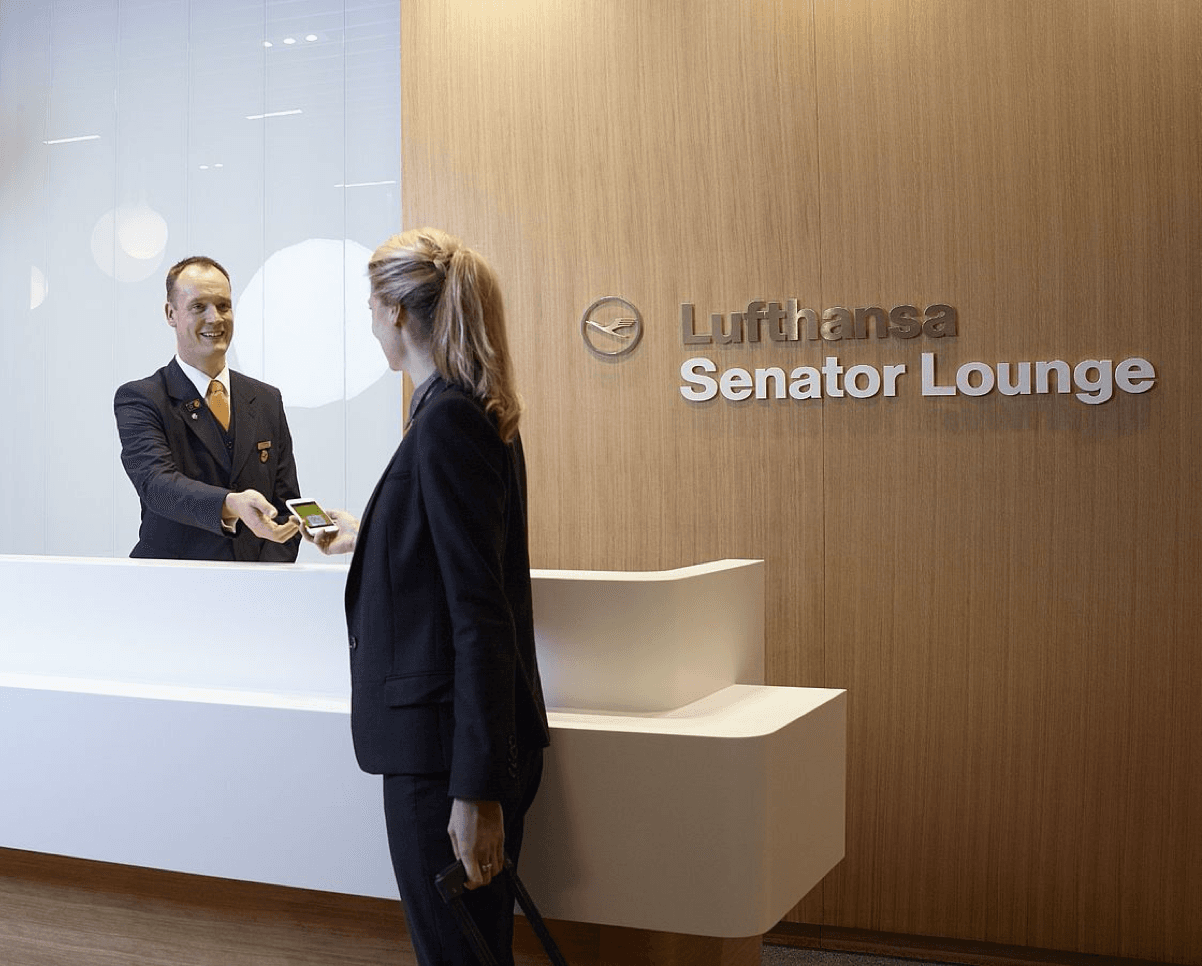 Staff member checking in a guest at the Lufthansa Senator Lounge reception desk with wooden wall backdrop.