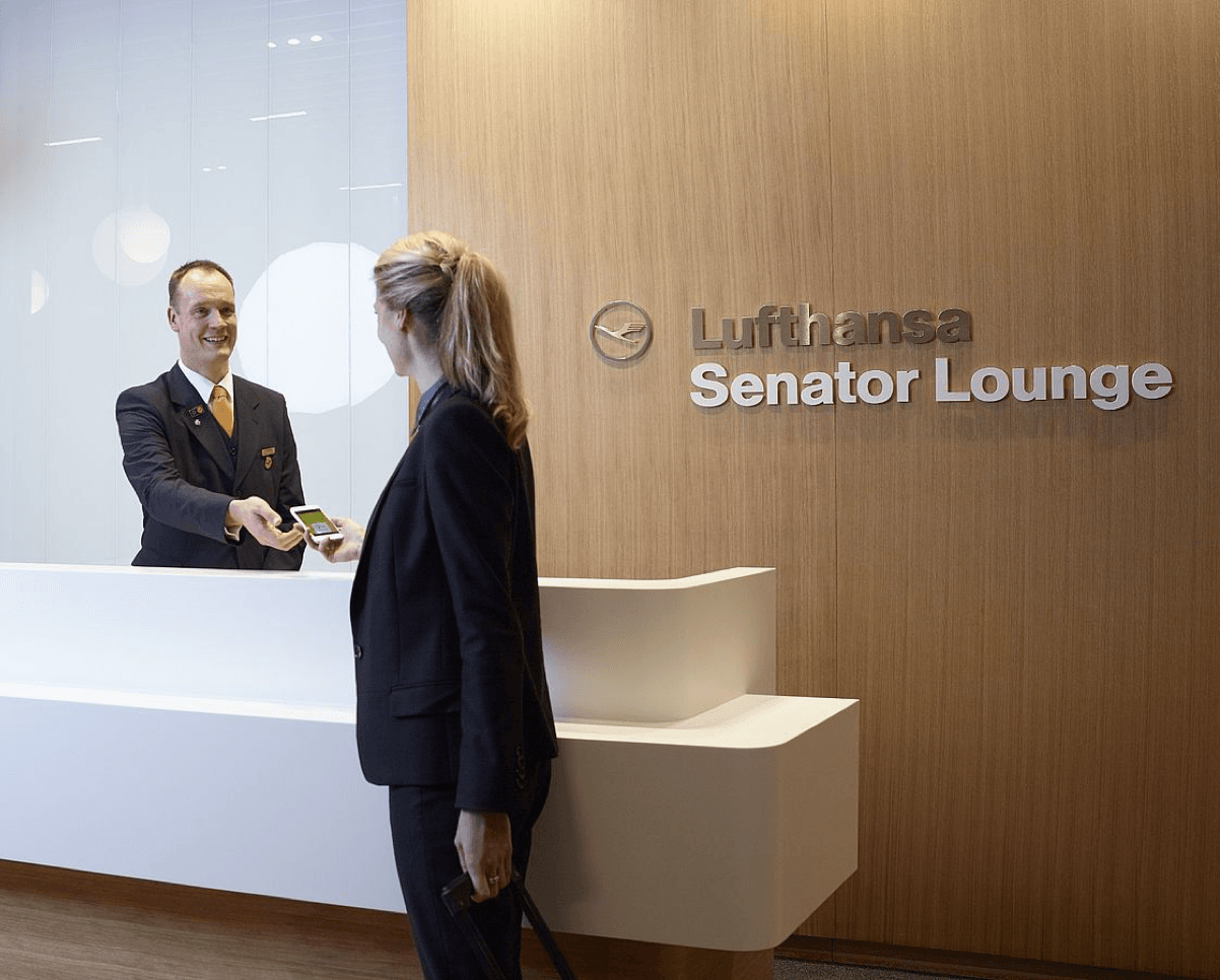 Staff member checking in a guest at the Lufthansa Senator Lounge reception desk with wooden wall backdrop.