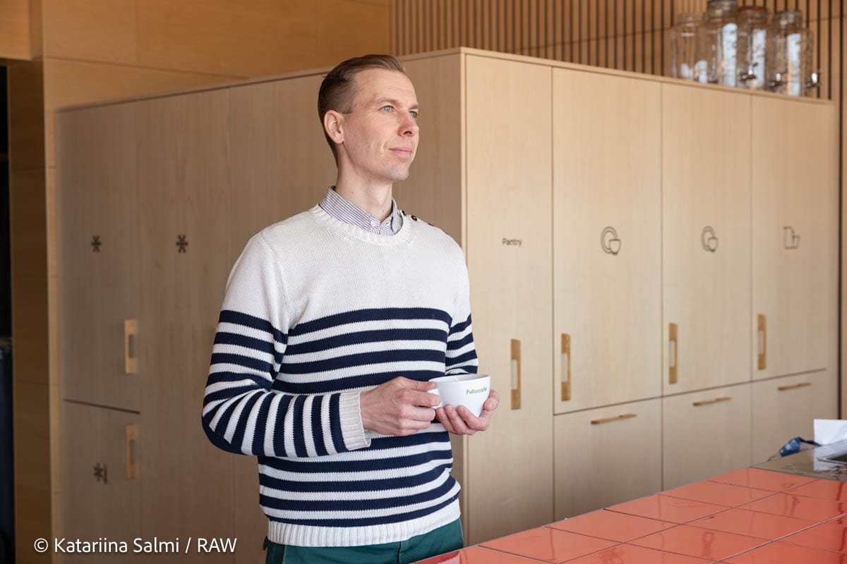 Person in striped navy and white jumper holding a white cup in modern kitchen with wooden cabinetry.