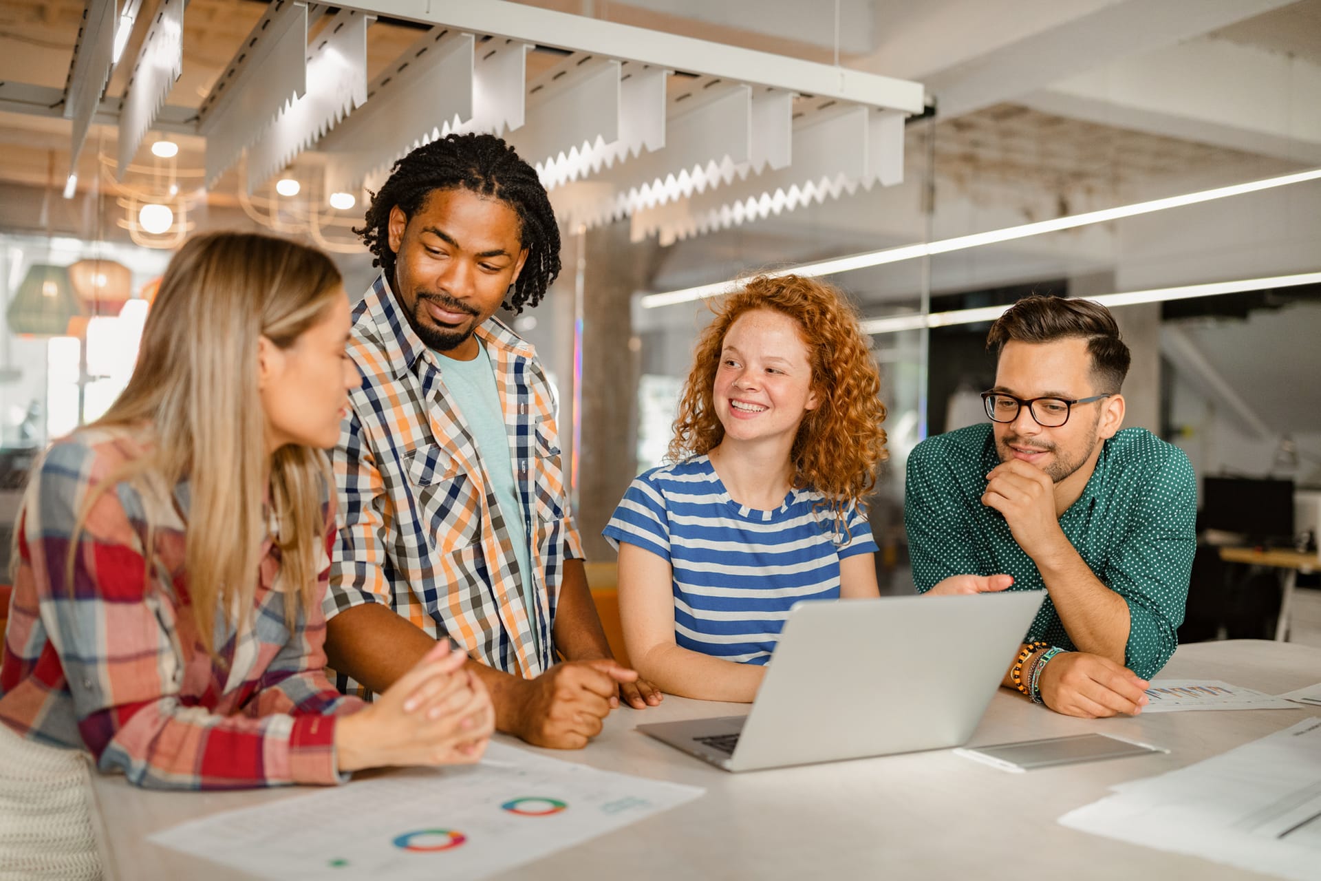 Diverse group of young professionals collaborating around a laptop in a modern, bright office space.