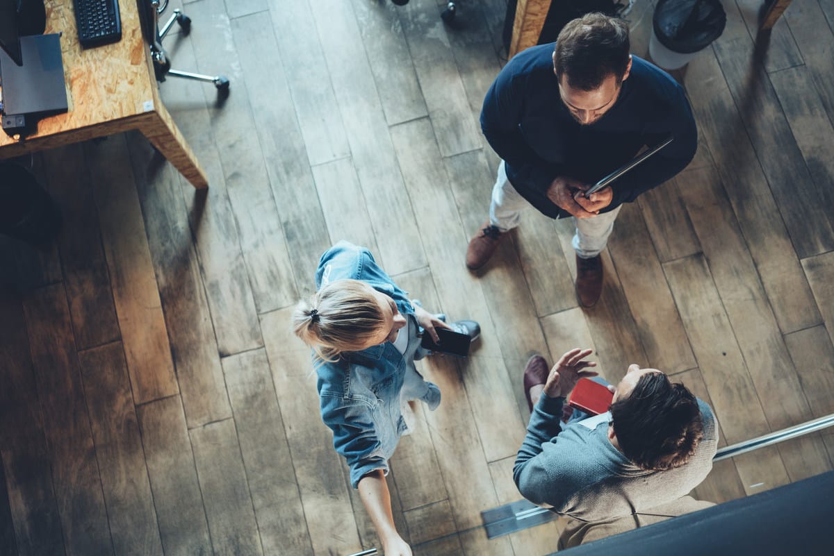 Overhead view of three people having a discussion on wooden flooring in a modern office space.