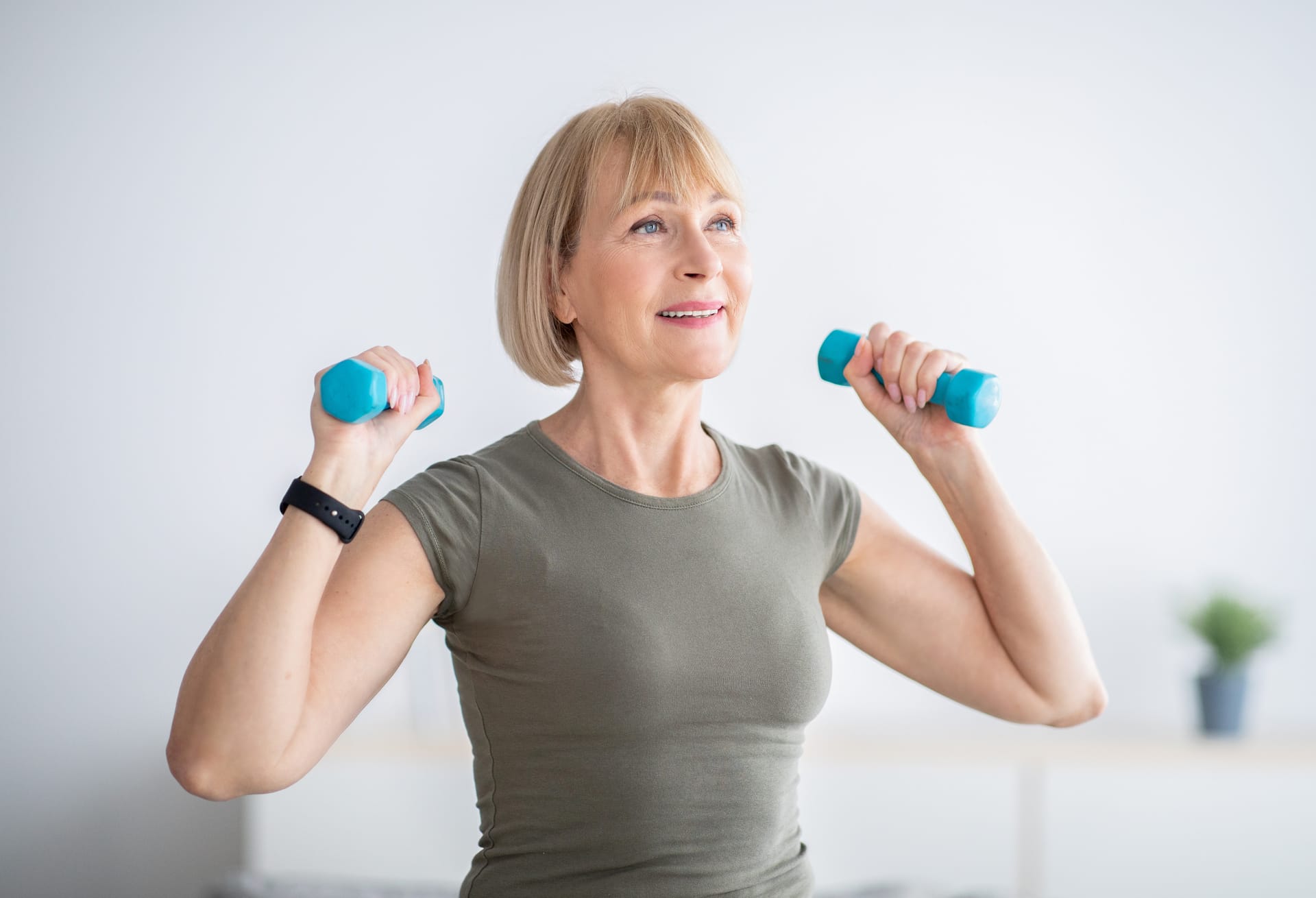 Person with blonde bob haircut exercising with turquoise dumbbells, wearing grey t-shirt and fitness tracker.