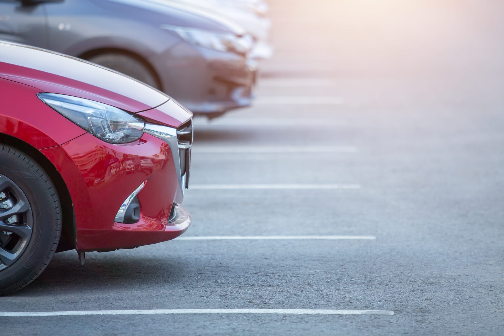 Front section of a glossy red car parked in a car park, with another vehicle visible in the background.