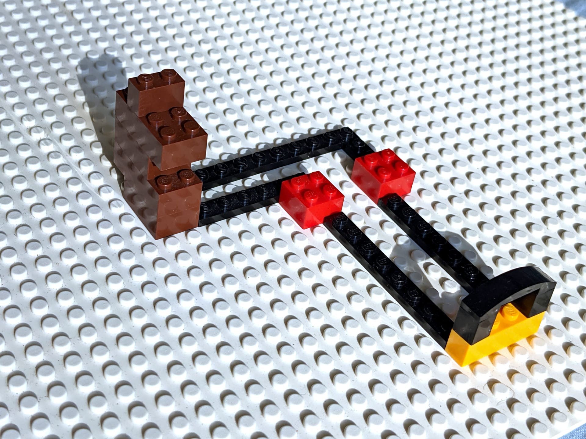 LEGO construction on white baseplate showing brown blocks connected to black beams with red and yellow pieces forming a simple structure.
