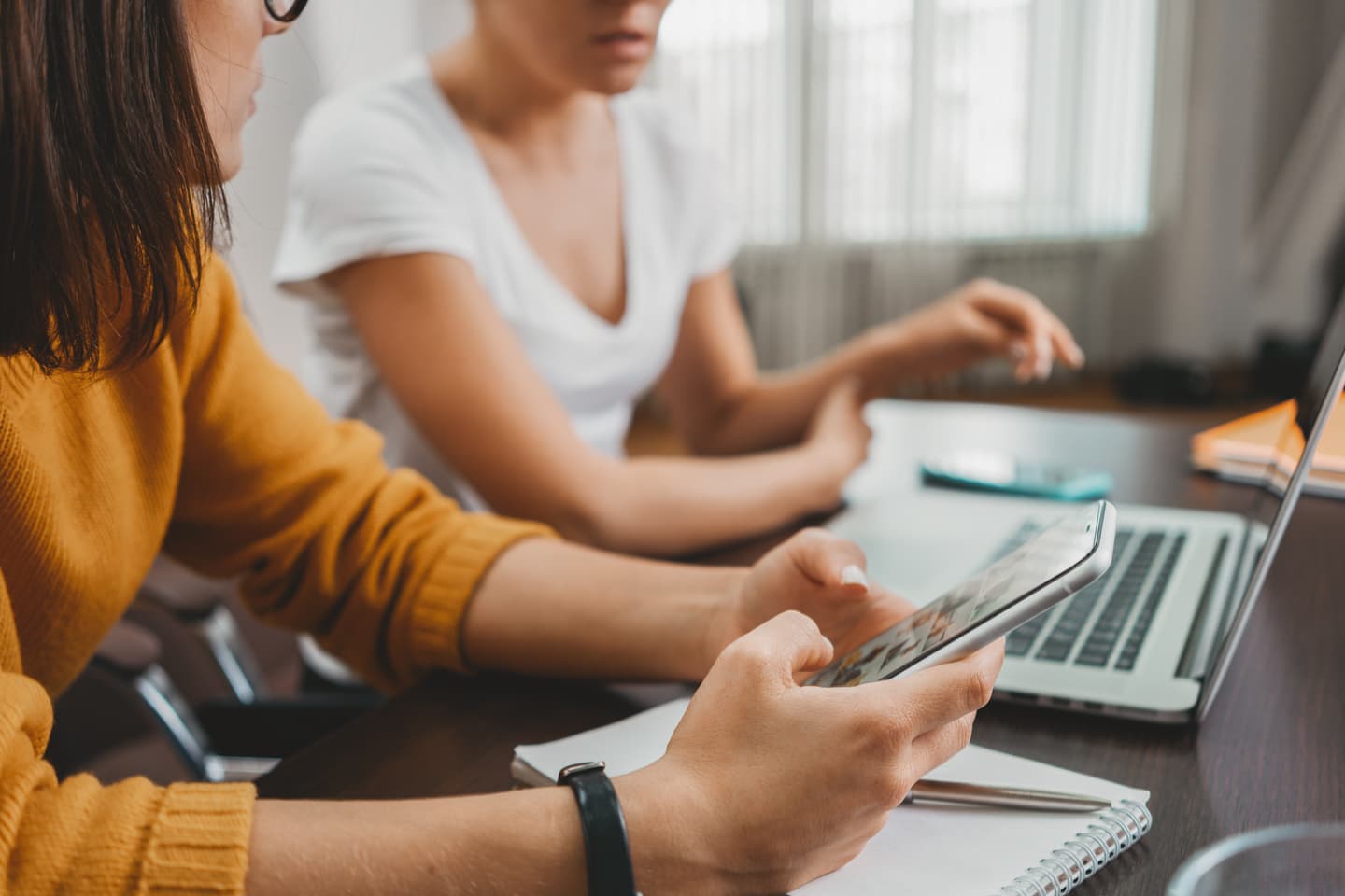 Two people working together at a desk, one using a tablet while the other types on a laptop.