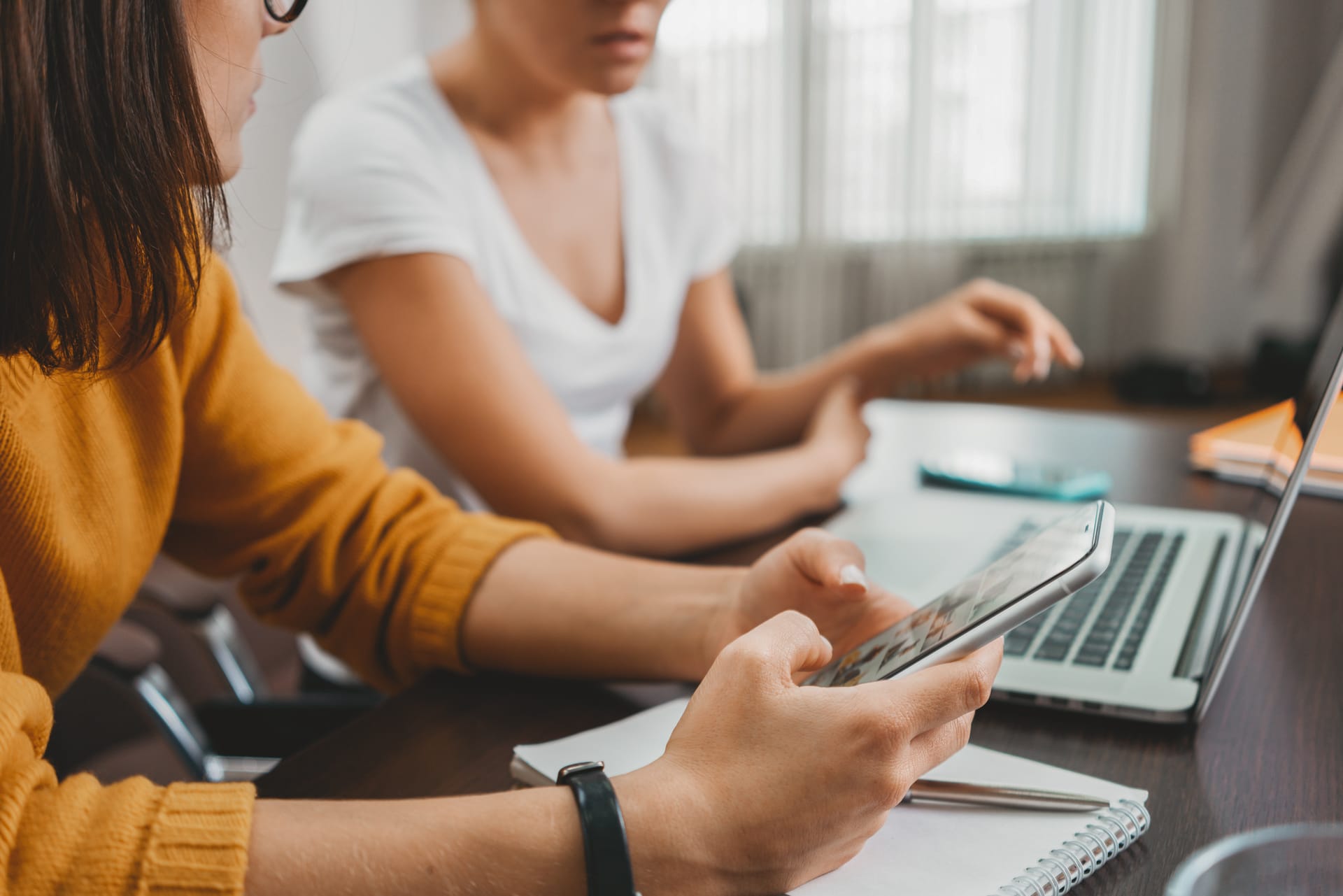 Two people working together at a desk, one using a tablet while the other types on a laptop.