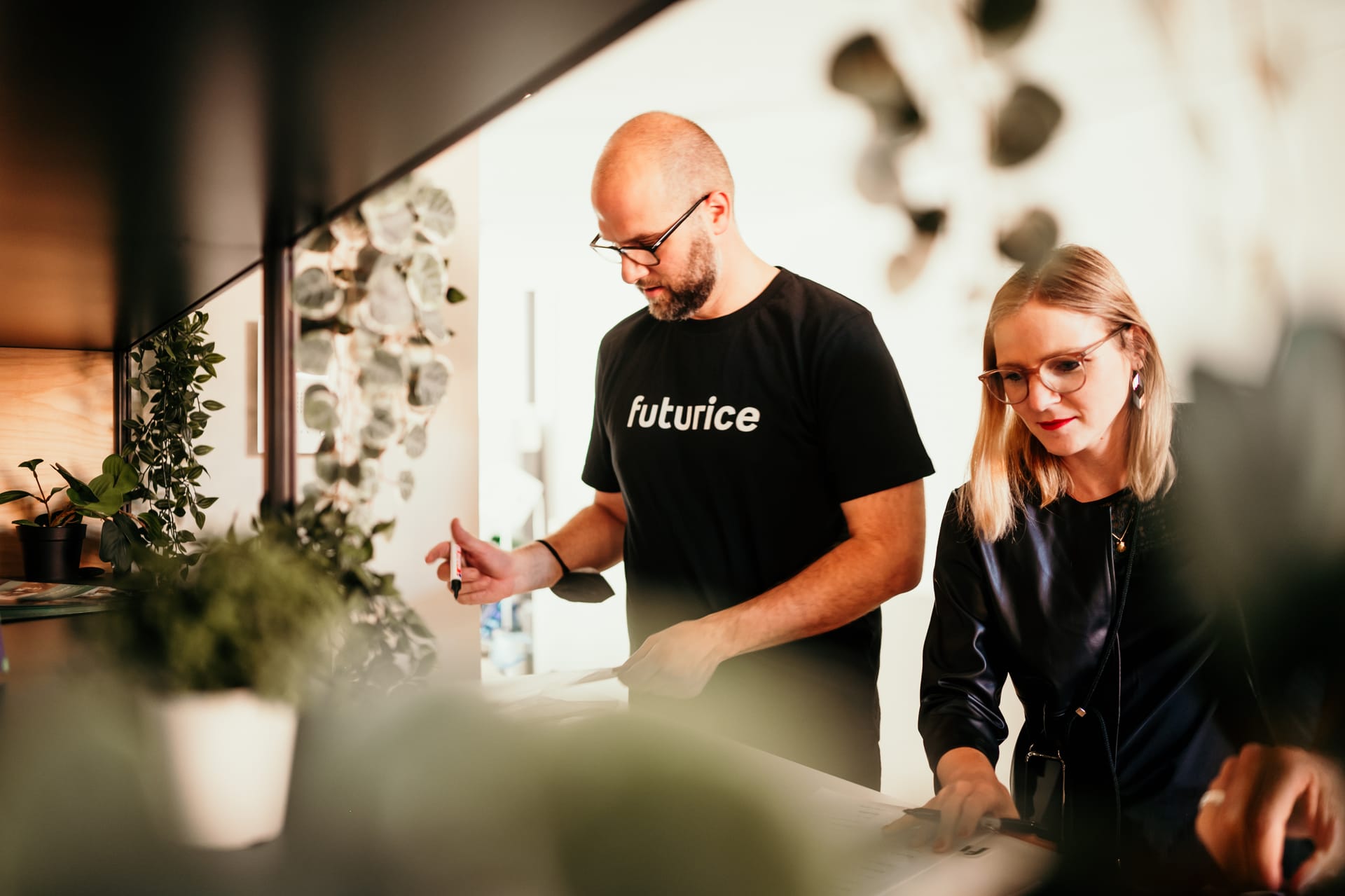 Two colleagues collaborating in a modern office space, man wearing "futurice" t-shirt and woman in black outfit.