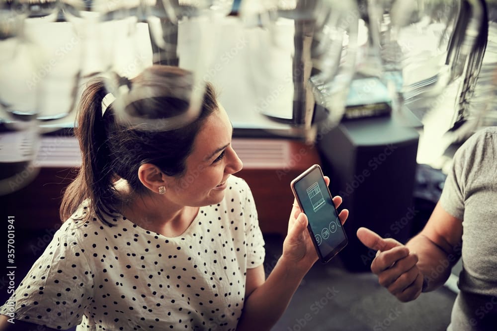 Woman in polka dot top looking at smartphone screen while conversing in a café setting.